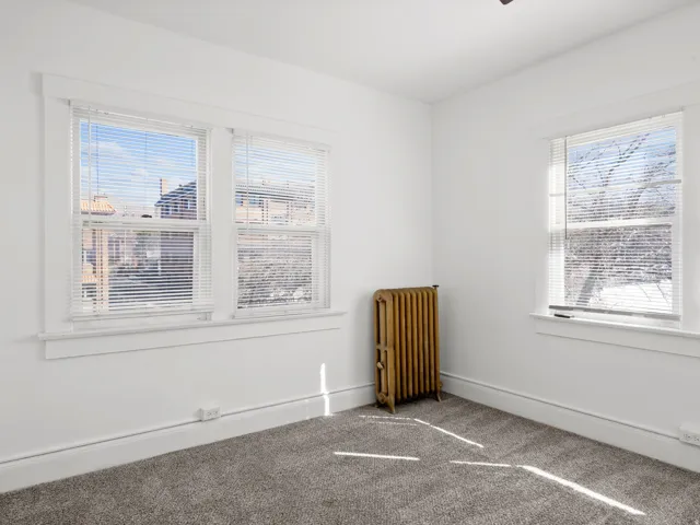 Empty room featuring radiator heating unit, carpet, and healthy amount of natural light