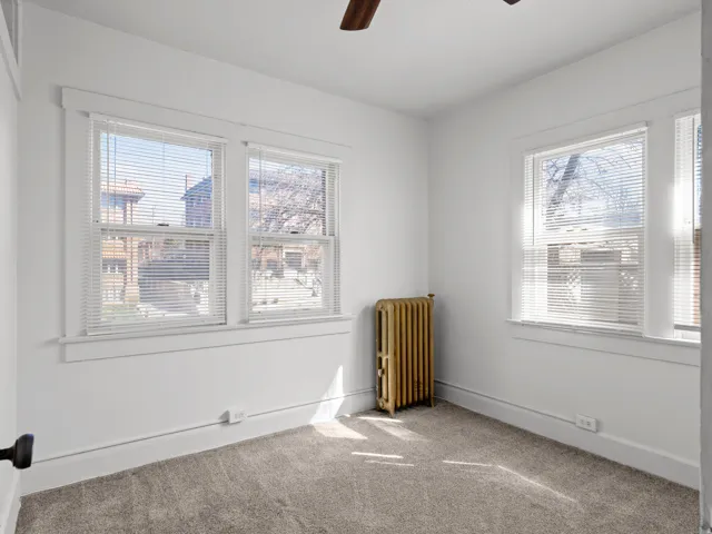 Spare room with a ceiling fan, radiator, carpet floors, and healthy amount of natural light