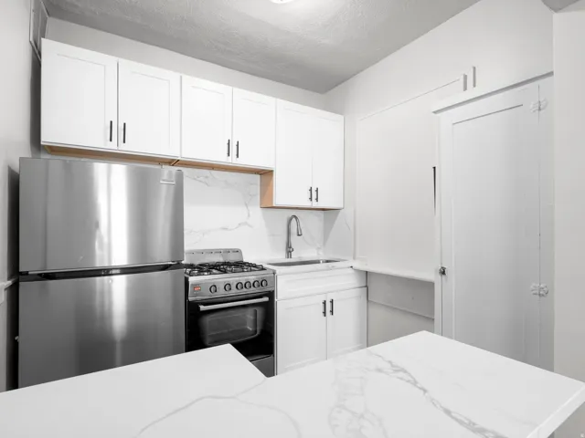 Kitchen featuring freestanding refrigerator, backsplash, range with gas cooktop, white cabinets, and light stone countertops