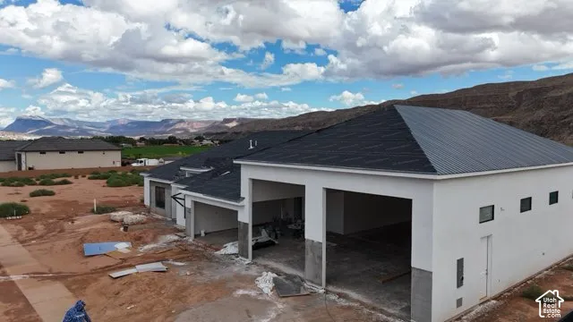 White stucco exterior, dark shingle roofing, exposed concrete foundation, recessed garage openings, multiple small rectangular windows