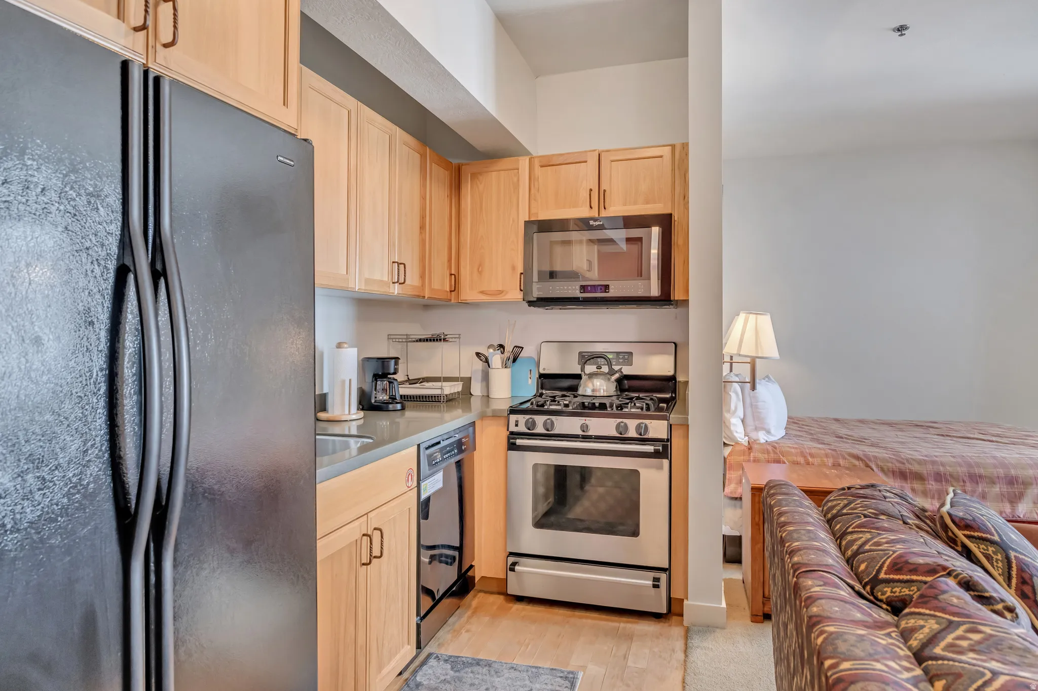 Kitchen with black appliances, light wood finish cabinetry, and light wood-style flooring