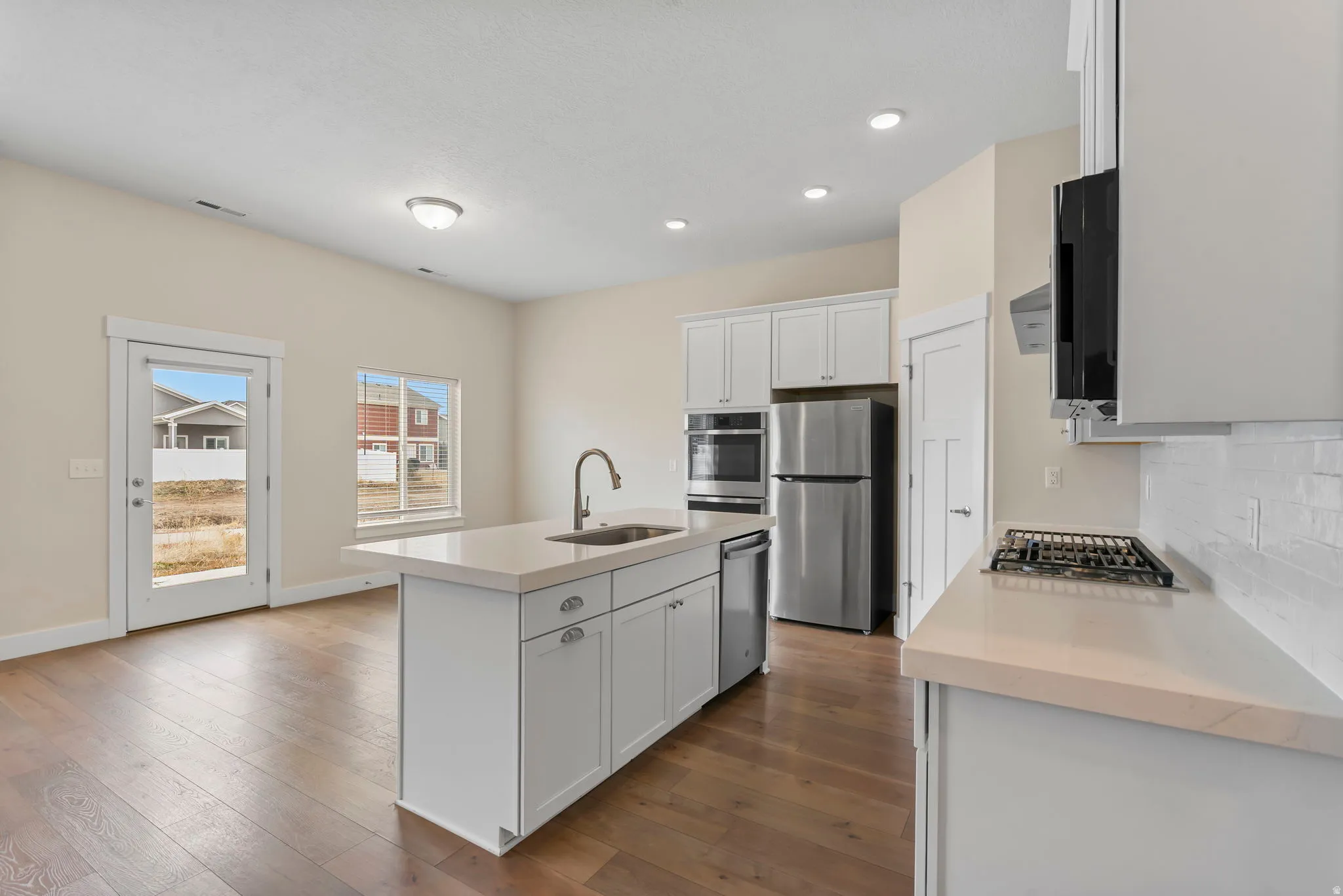 Kitchen featuring a kitchen island with sink, stainless steel appliances, white cabinetry, dark wood-style flooring, and tasteful backsplash