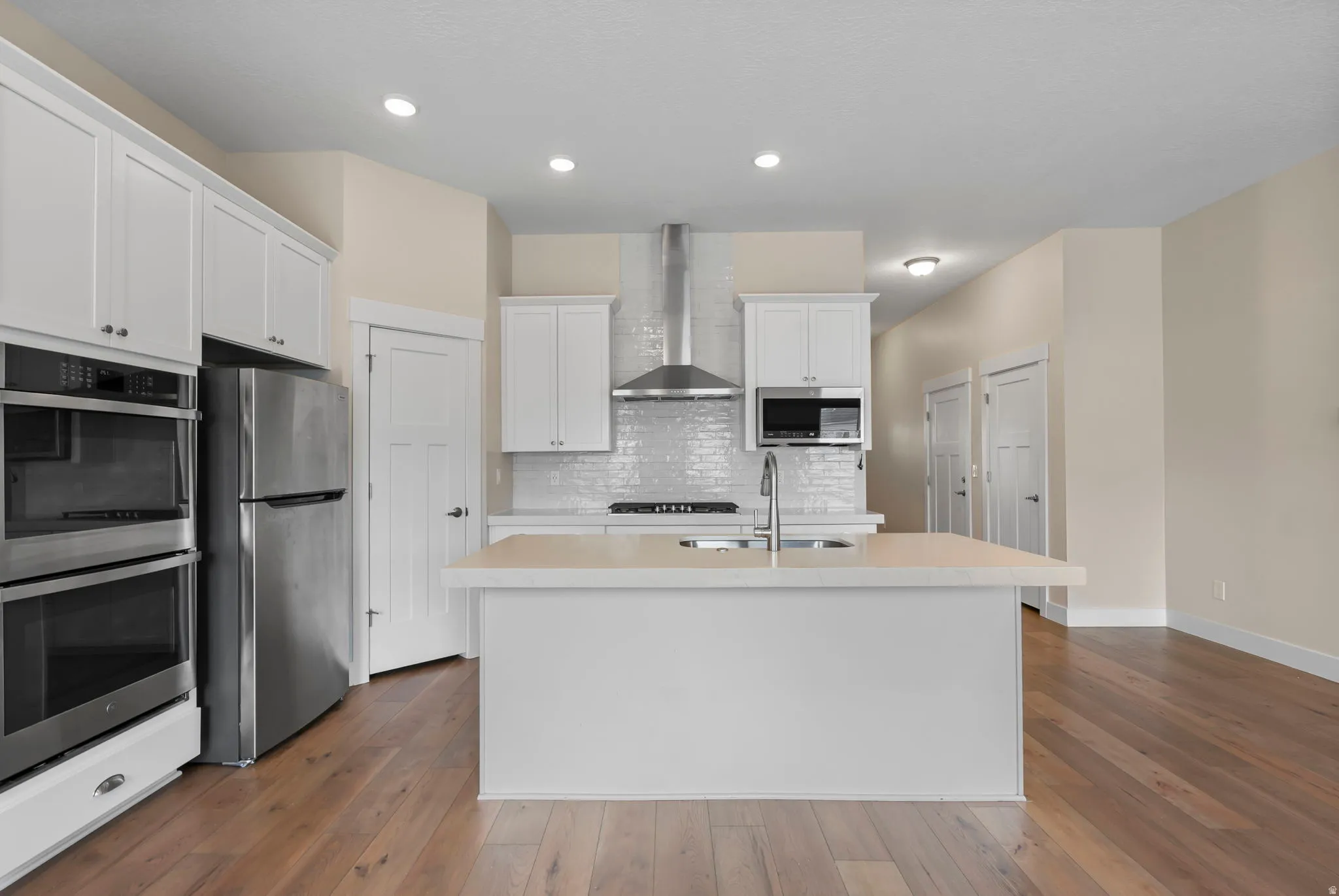 Kitchen with stainless steel appliances, light countertops, white cabinetry, dark wood-style flooring, and recessed lighting