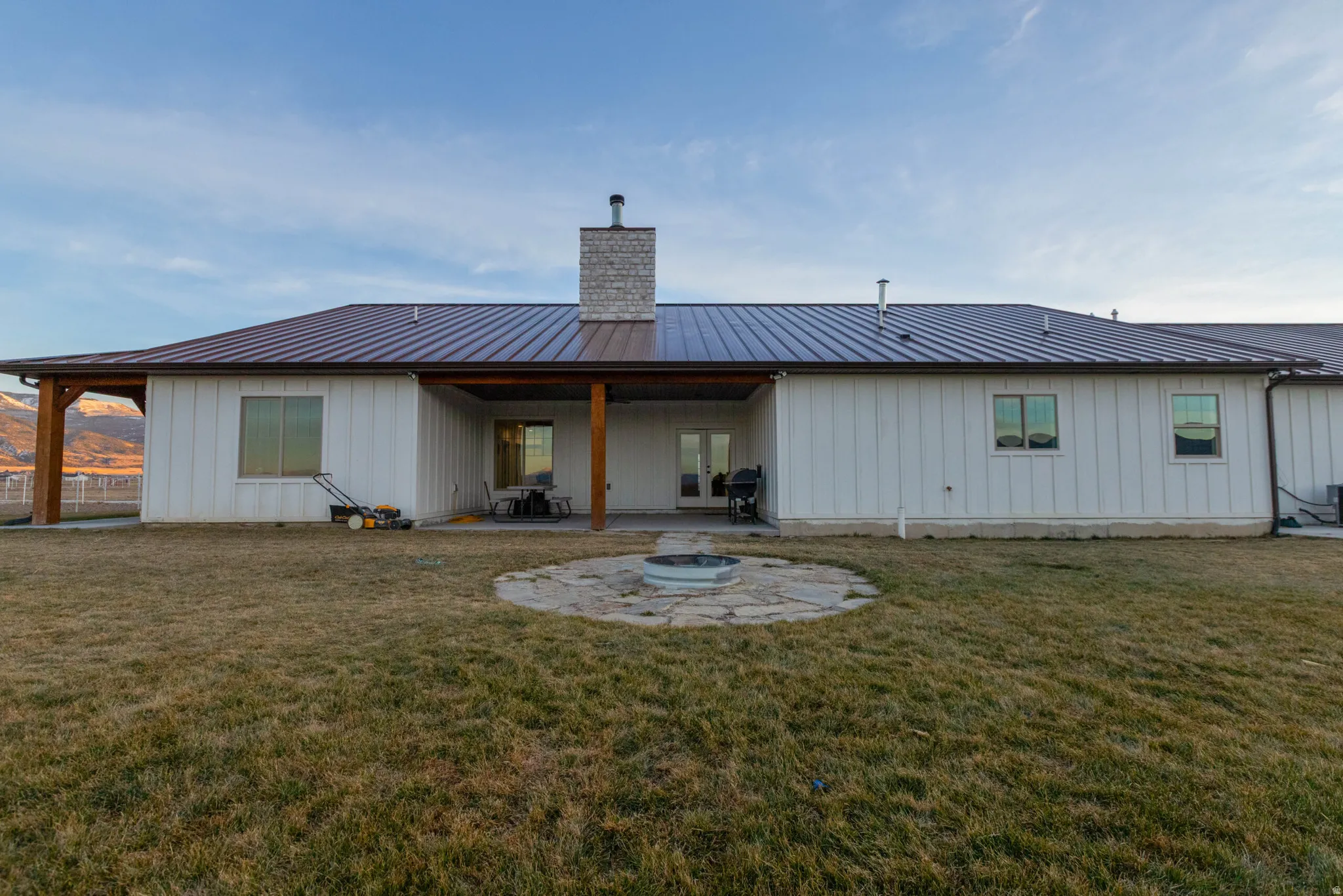 Rear view of property with a patio, board and batten siding, a metal roof, a yard, and a chimney
