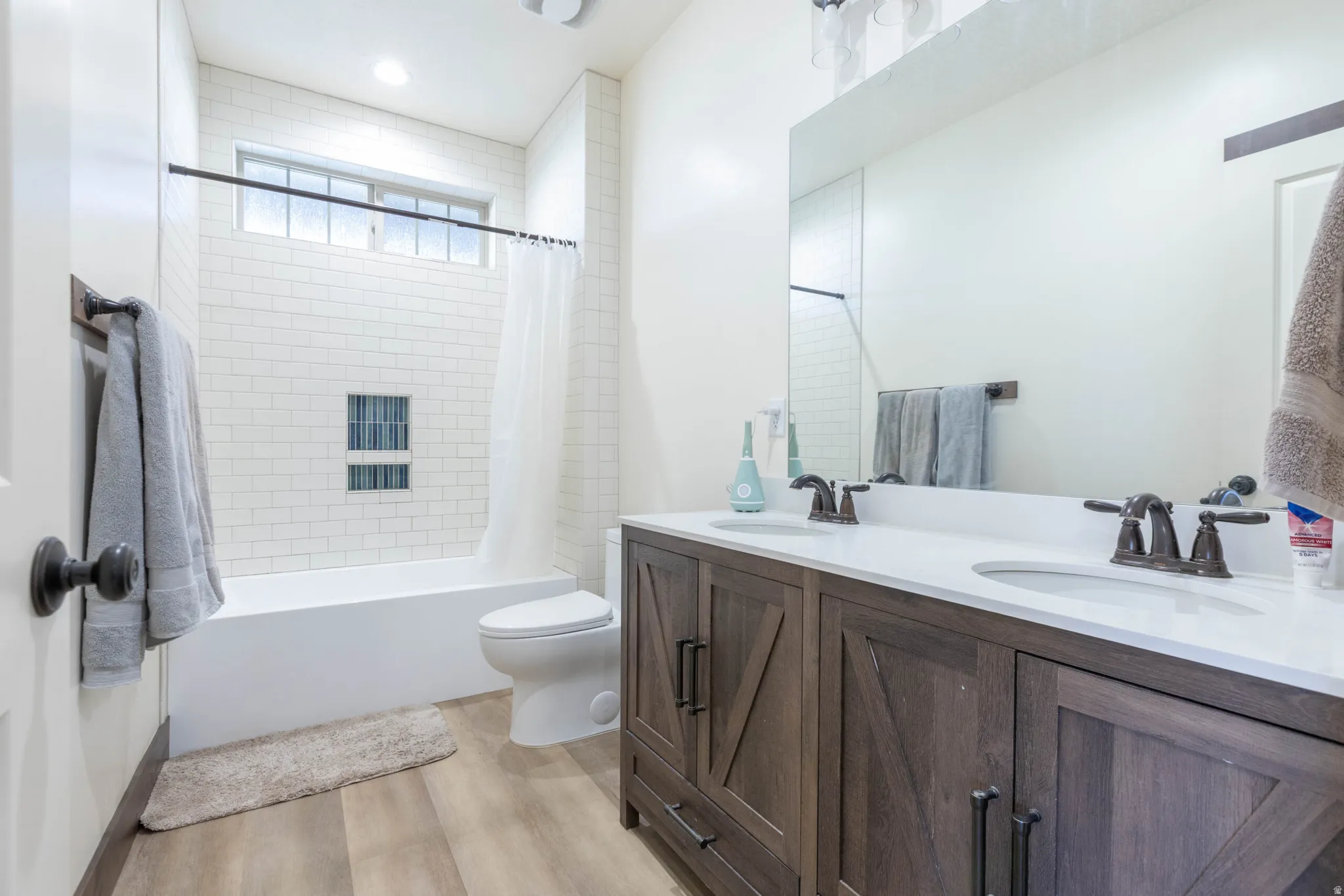 Full bath with double vanity, shower / bath combo, and light wood-style floors