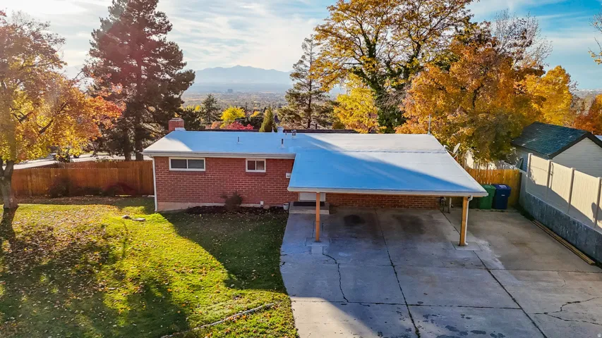 Rear view of house featuring a carport, concrete driveway, brick siding, and a chimney