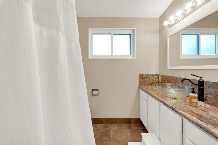 Bathroom with vanity, a shower with shower curtain, and dark stone finish floors