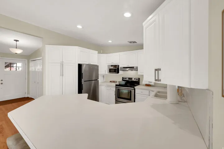 Kitchen featuring stainless steel appliances, light countertops, white cabinets, lofted ceiling, and light wood-type flooring