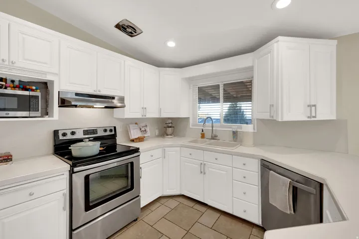 Kitchen featuring stainless steel appliances, white cabinetry, recessed lighting, light tile patterned floors, and vaulted ceiling