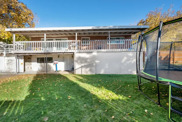 Rear view of house featuring a yard, a trampoline, brick siding, and a balcony