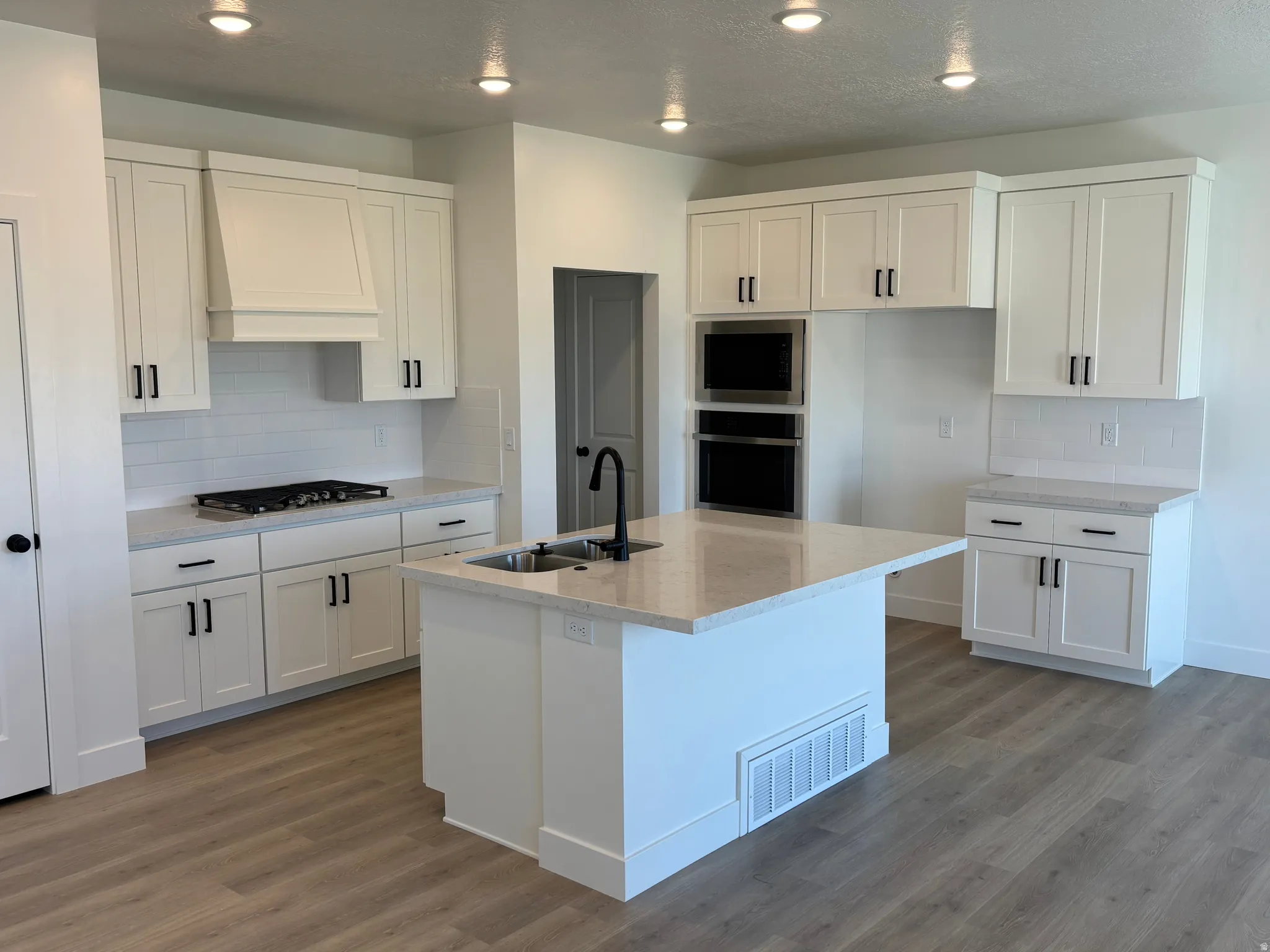 Kitchen featuring decorative backsplash, light stone countertops, light wood-type flooring, stainless steel appliances, and recessed lighting