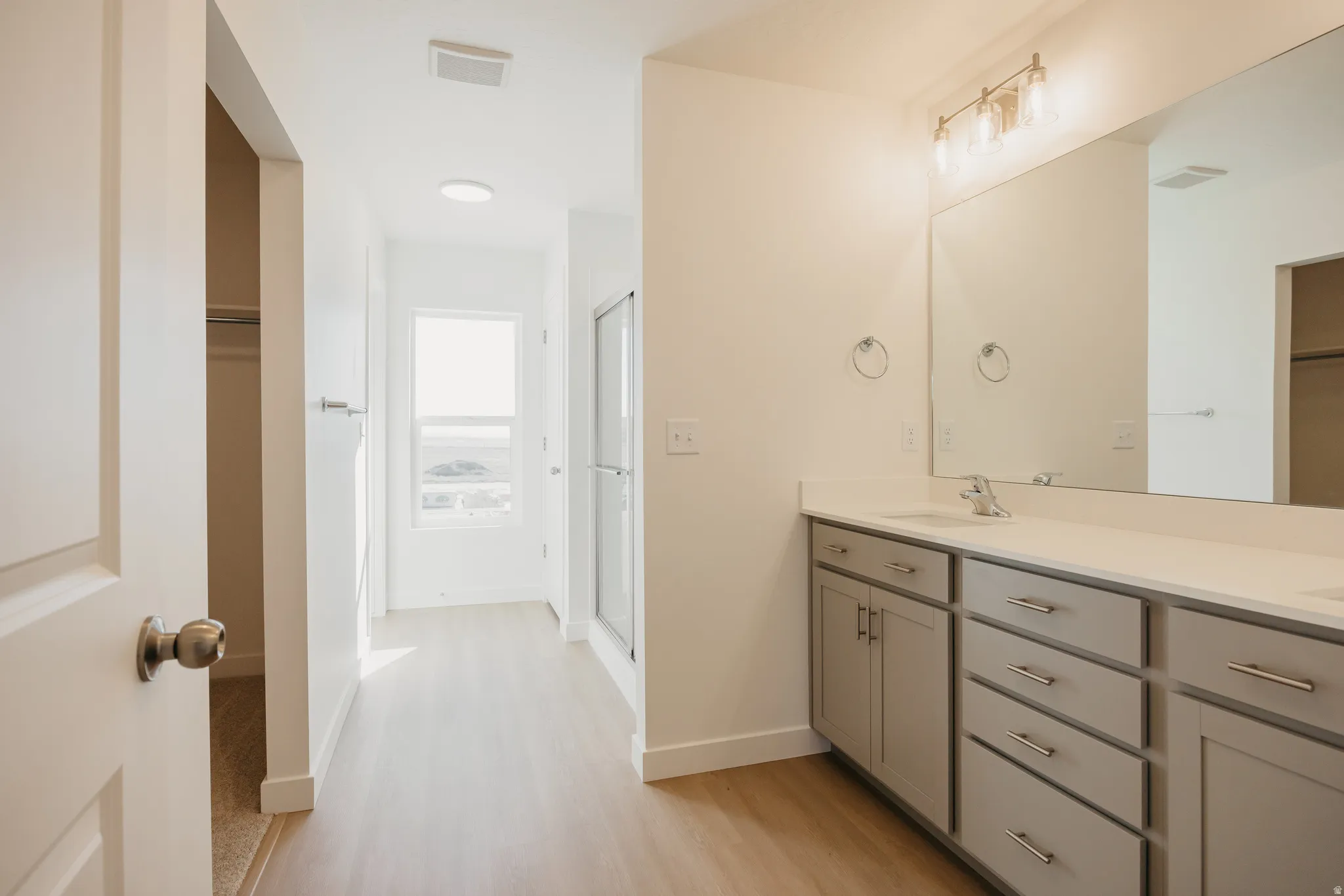 Full bath with a walk in closet, double vanity, a shower stall, and light wood-style flooring