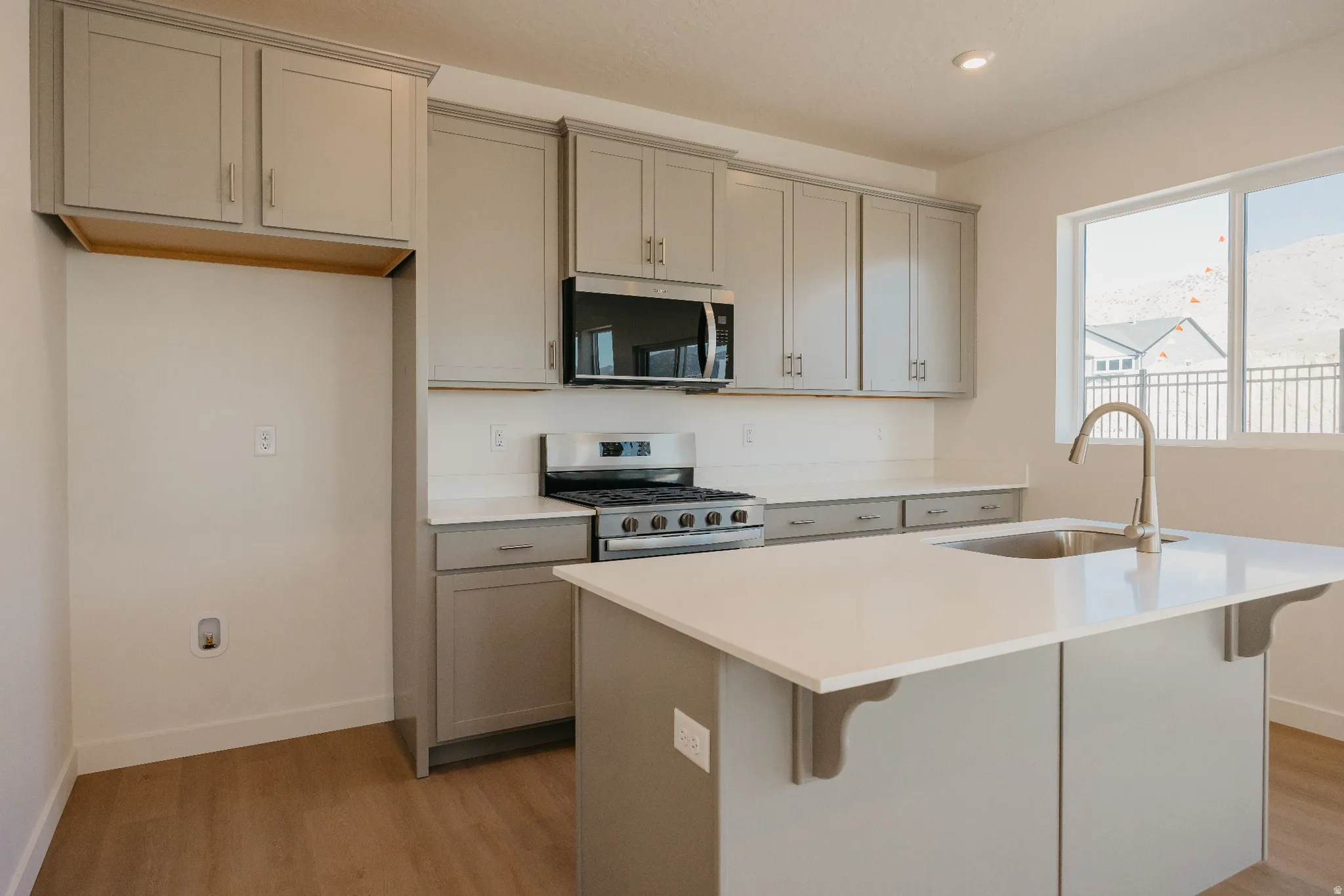 Kitchen featuring gray cabinetry, stainless steel appliances, an island with sink, a breakfast bar area, and light wood finished floors