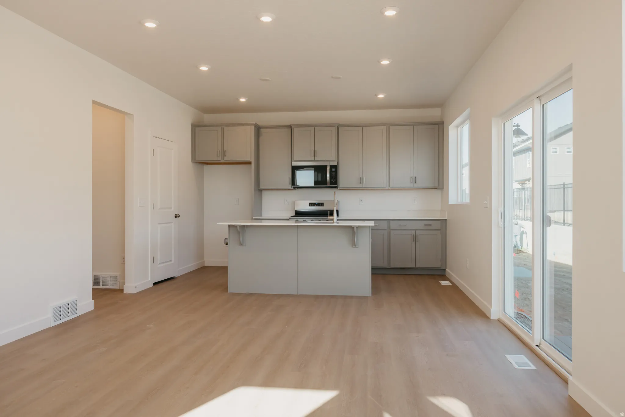 Kitchen with gray cabinets, light countertops, a breakfast bar area, recessed lighting, and a kitchen island with sink