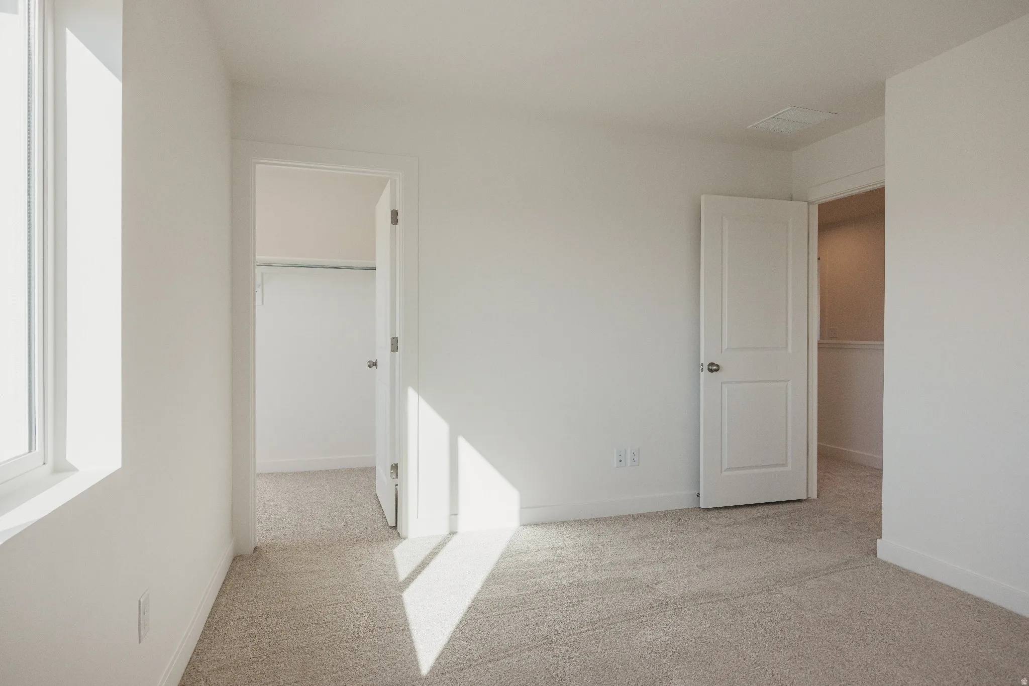 Unfurnished bedroom featuring a walk in closet and light colored carpet