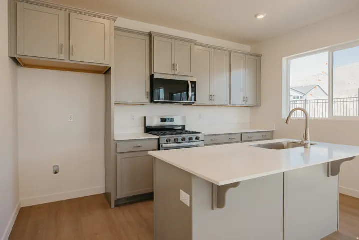 Kitchen featuring gray cabinetry, stainless steel appliances, an island with sink, a breakfast bar area, and light wood finished floors