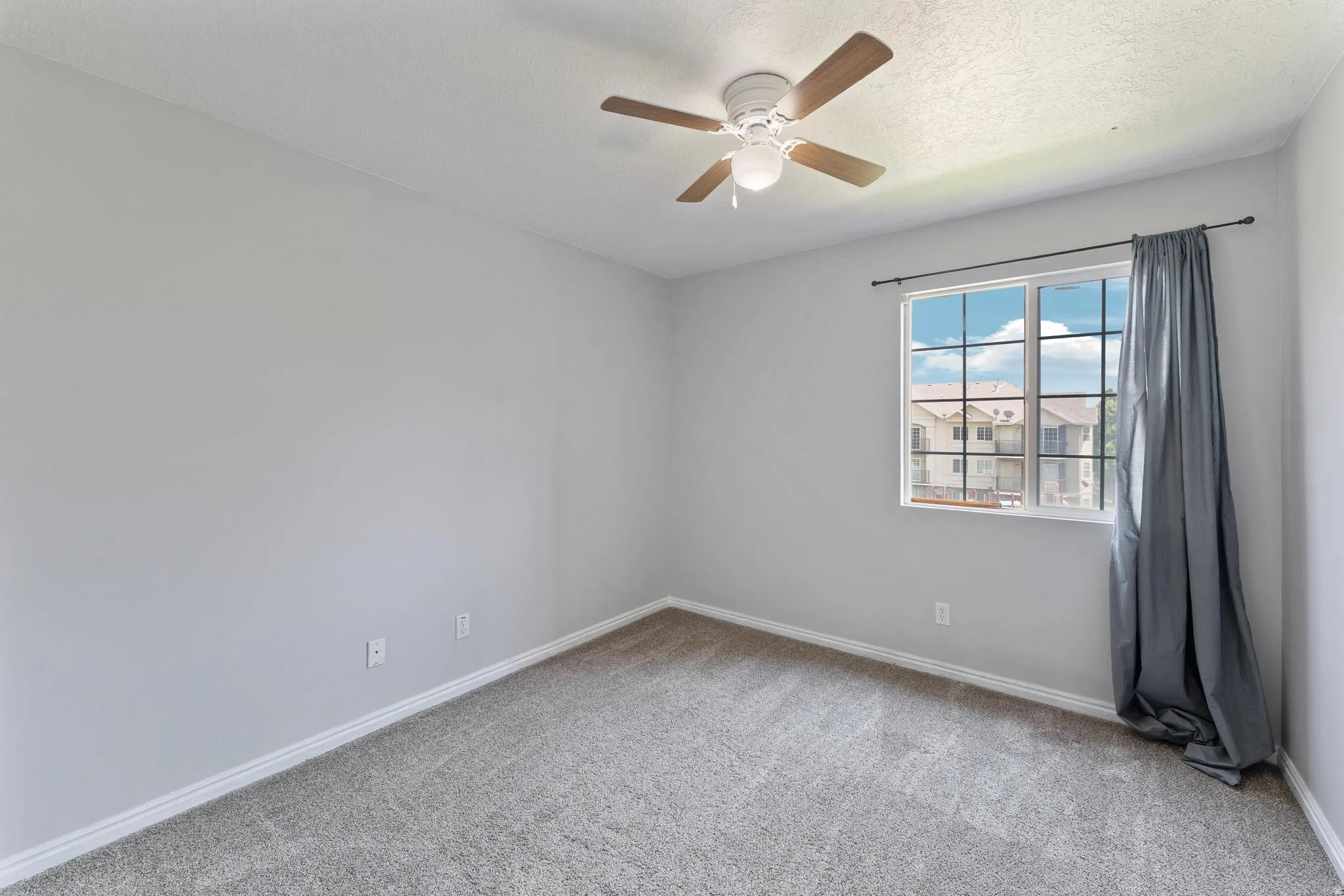 Empty room with light colored carpet, ceiling fan, and a textured ceiling