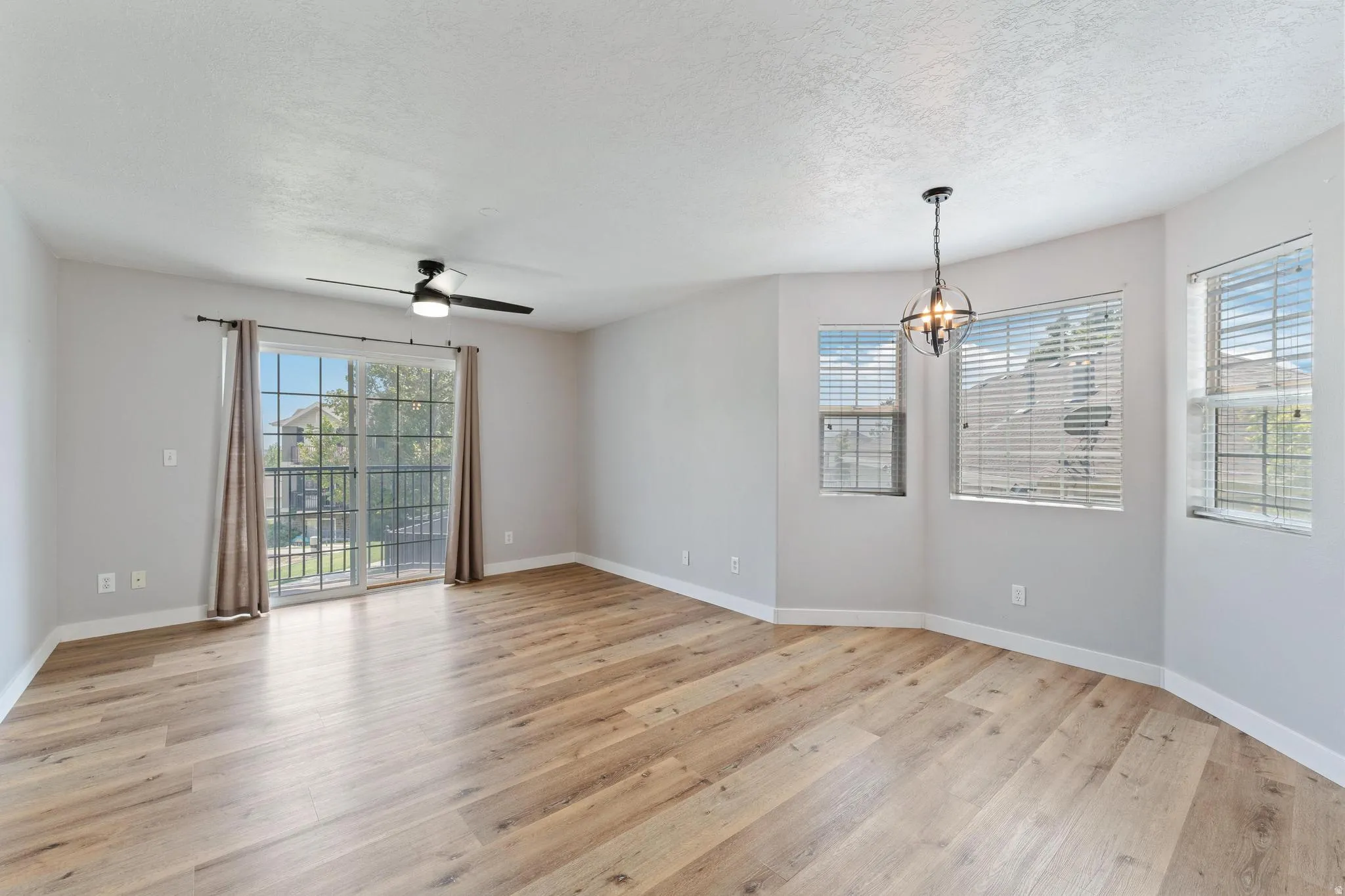 Spare room featuring light wood finished floors, a ceiling fan, plenty of natural light, a textured ceiling, and suspended lighting