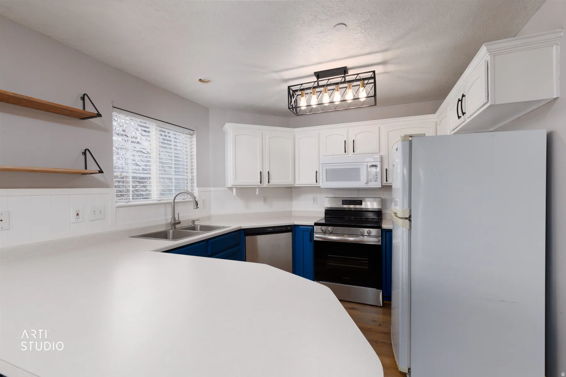 Dual tone kitchen with stainless steel appliances, two tone cabinetry, light countertops, open shelves, and dark wood finished floors