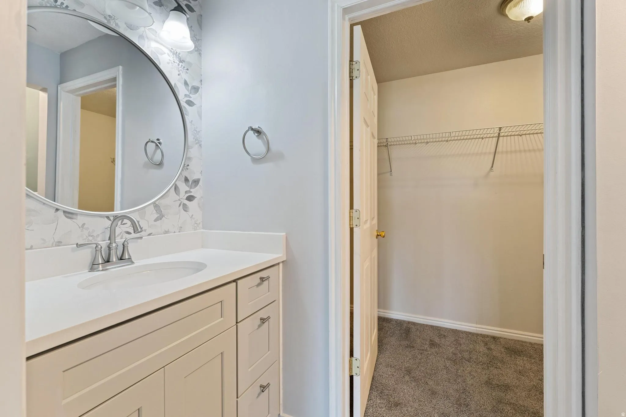 Bathroom featuring a spacious closet, vanity, dark carpet, and a textured ceiling