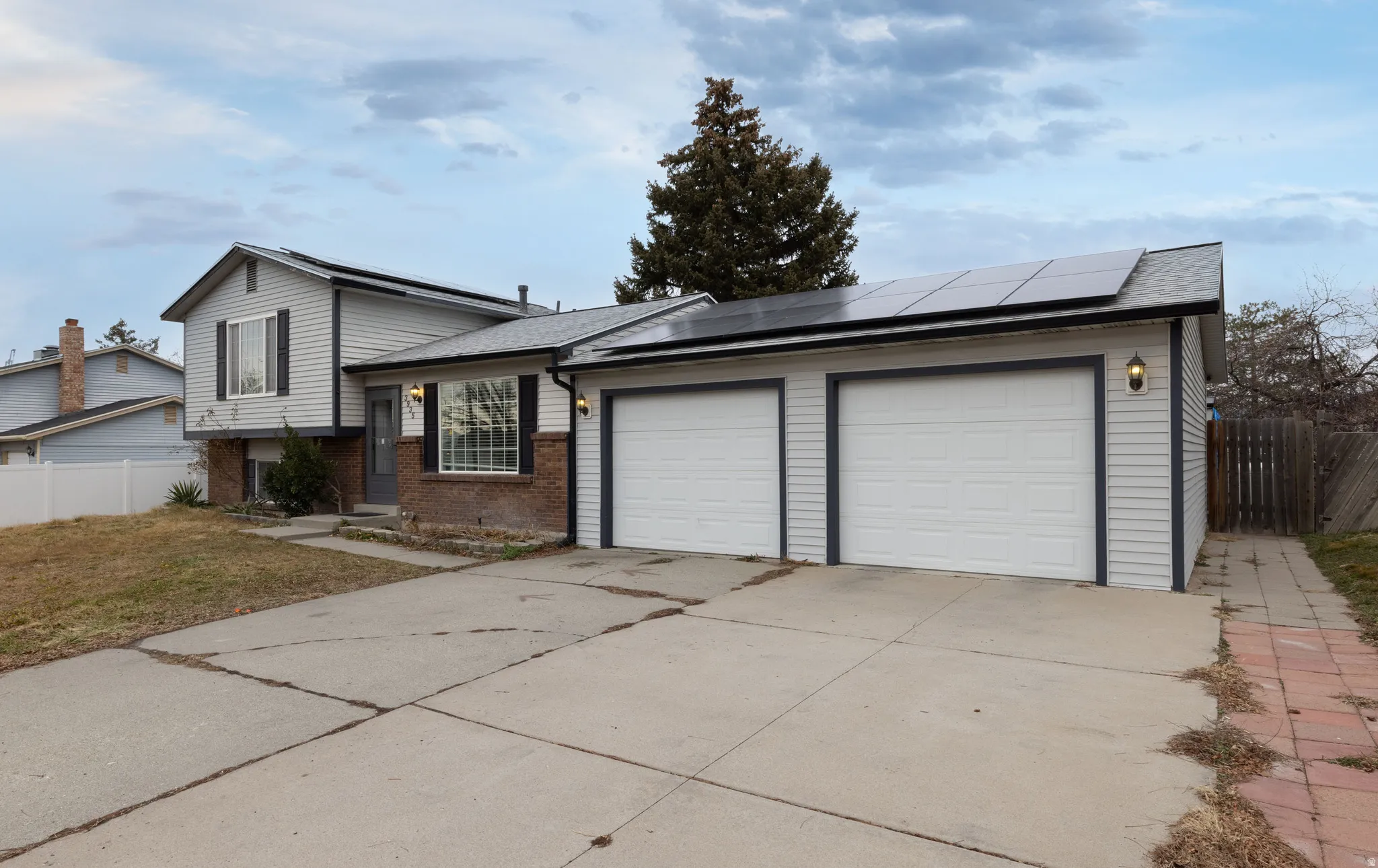 Split level home featuring brick siding, solar panels, concrete driveway, roof with shingles, and a 2 car garage