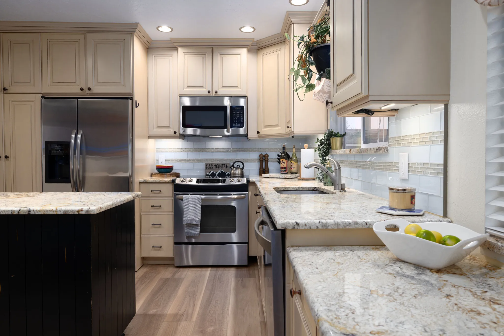Kitchen featuring stainless steel appliances, light granite stone countertops, cream cabinets, new light LVP wood-style floors, and backsplash