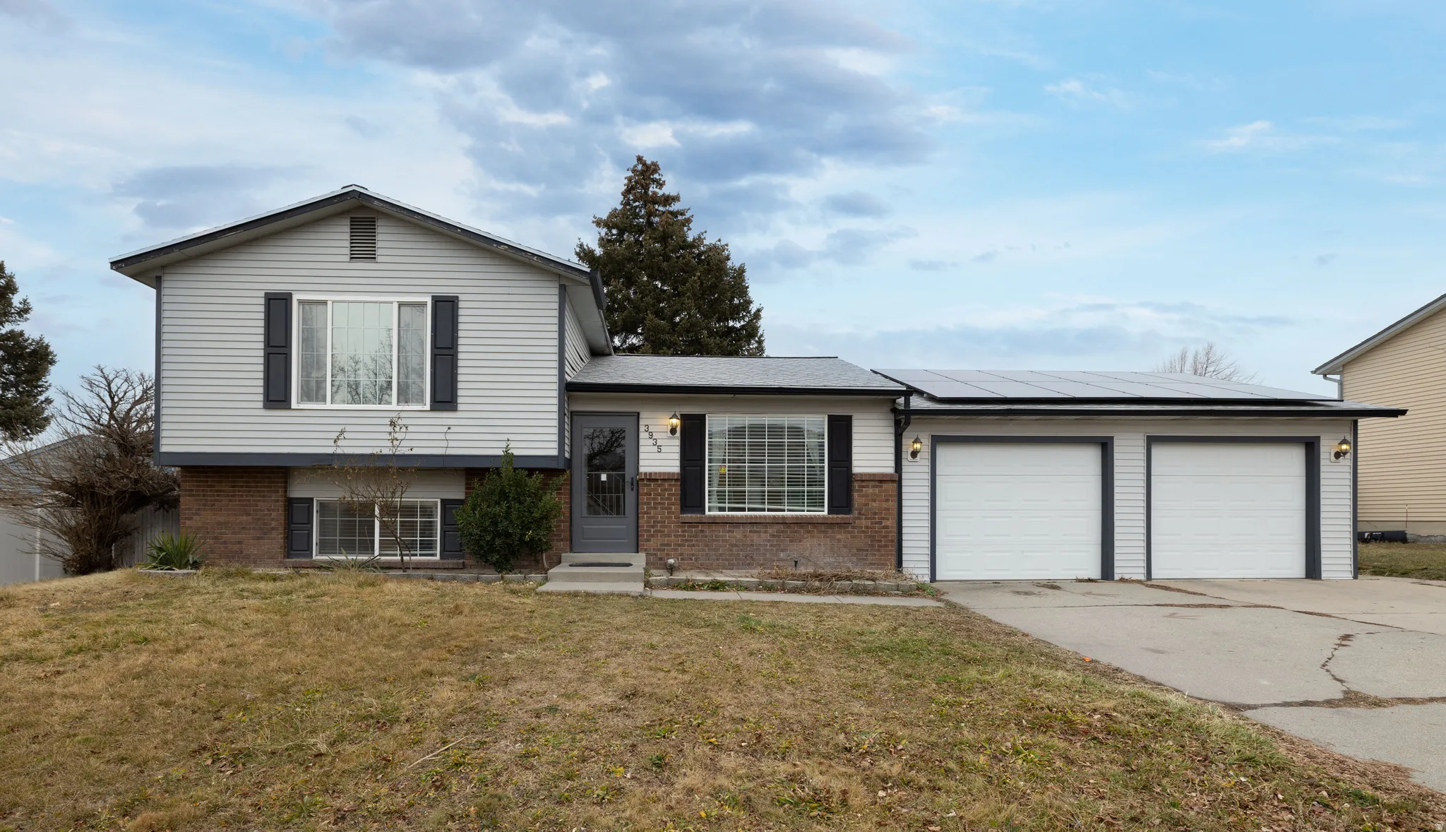 Split level home featuring brick siding, a front lawn, driveway, 2 car garage, and roof mounted solar panels