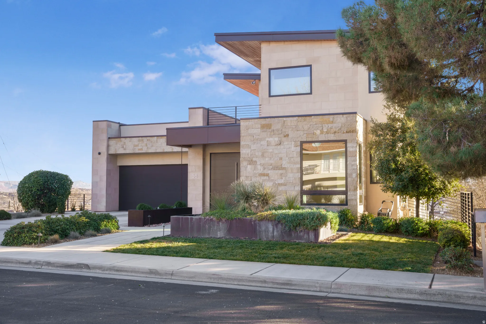 Modern home with a garage, stone siding, a front yard, and driveway