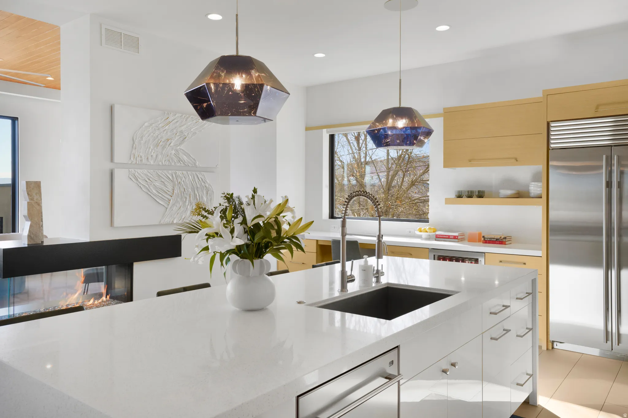 Kitchen featuring built in fridge, modern cabinets, light stone counters, pendant lighting, and light wood finish cabinetry
