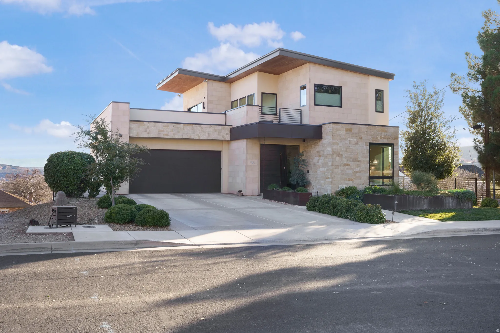 Modern home featuring a balcony, concrete driveway, stone siding, stucco siding, and an attached garage