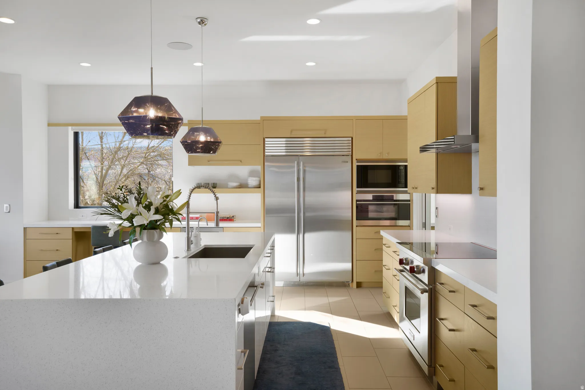 Kitchen featuring light wood finish cabinetry, built in appliances, pendant lighting, and modern cabinets