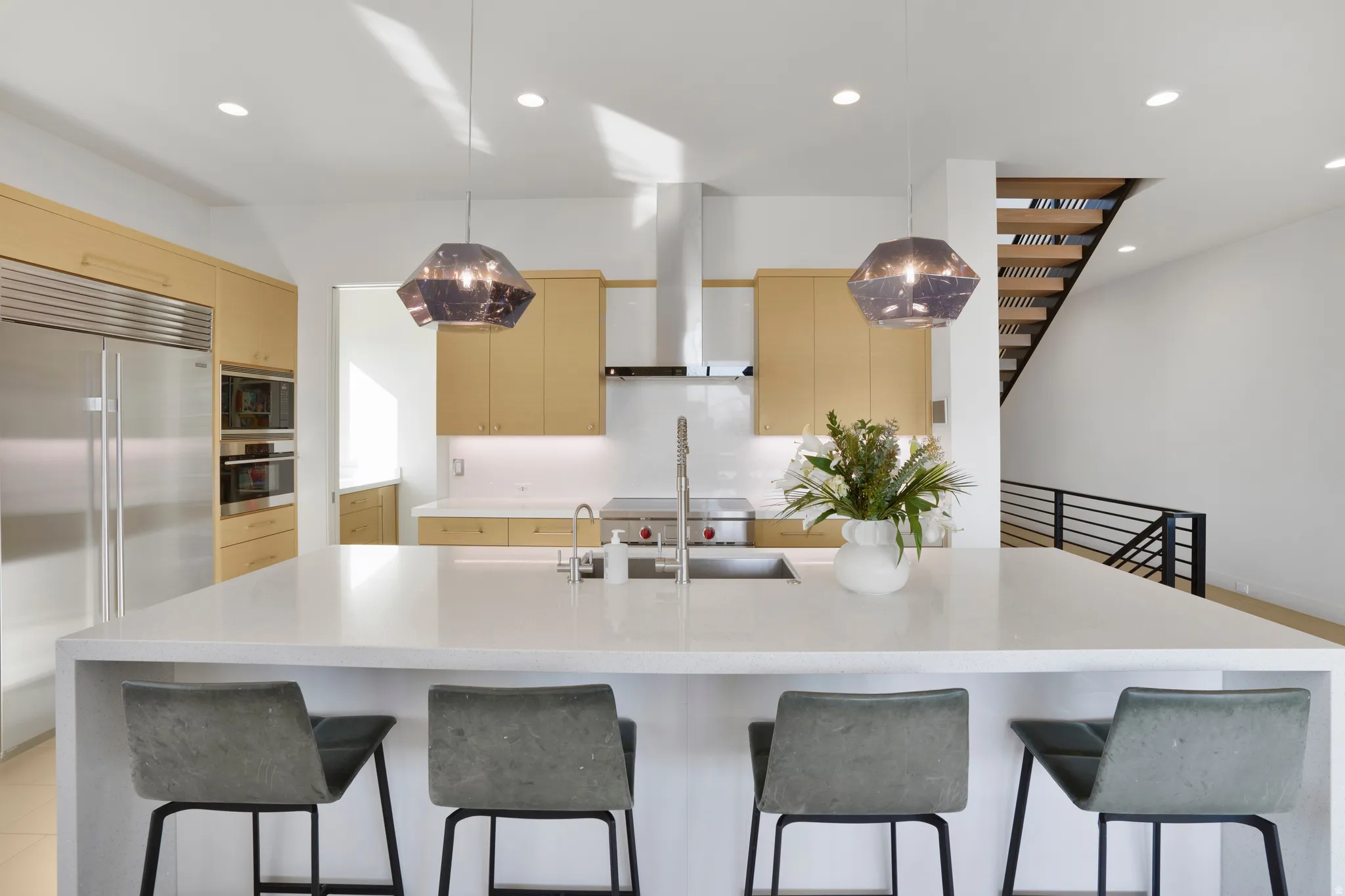 Kitchen with built in appliances, light stone counters, hanging light fixtures, a large island with sink, and a kitchen breakfast bar