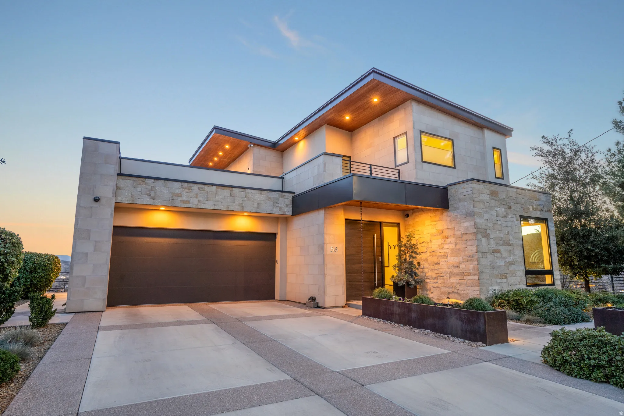 Contemporary house featuring a balcony, driveway, a garage, and stone siding