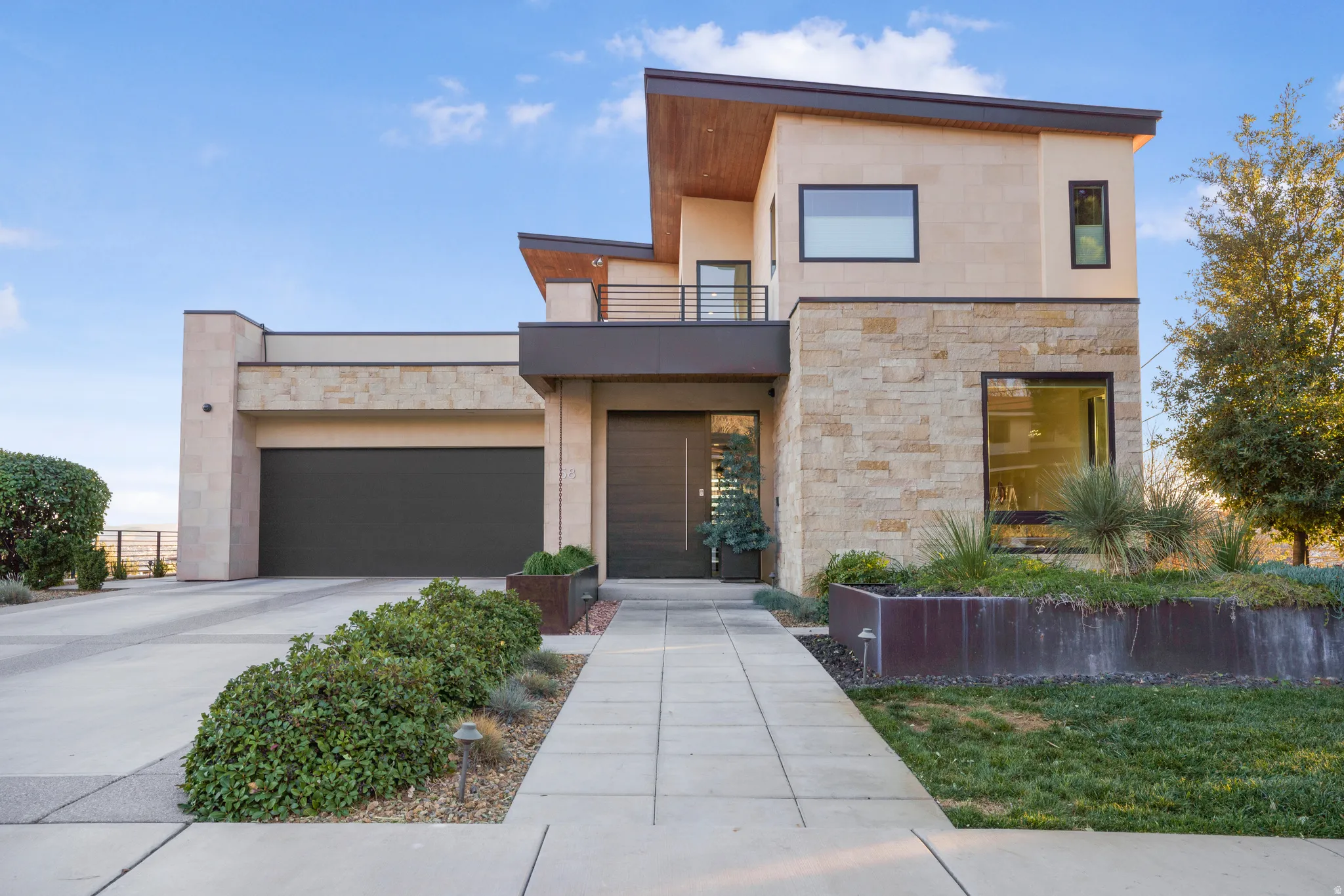 Modern home featuring stone siding, a balcony, driveway, an attached garage, and stucco siding