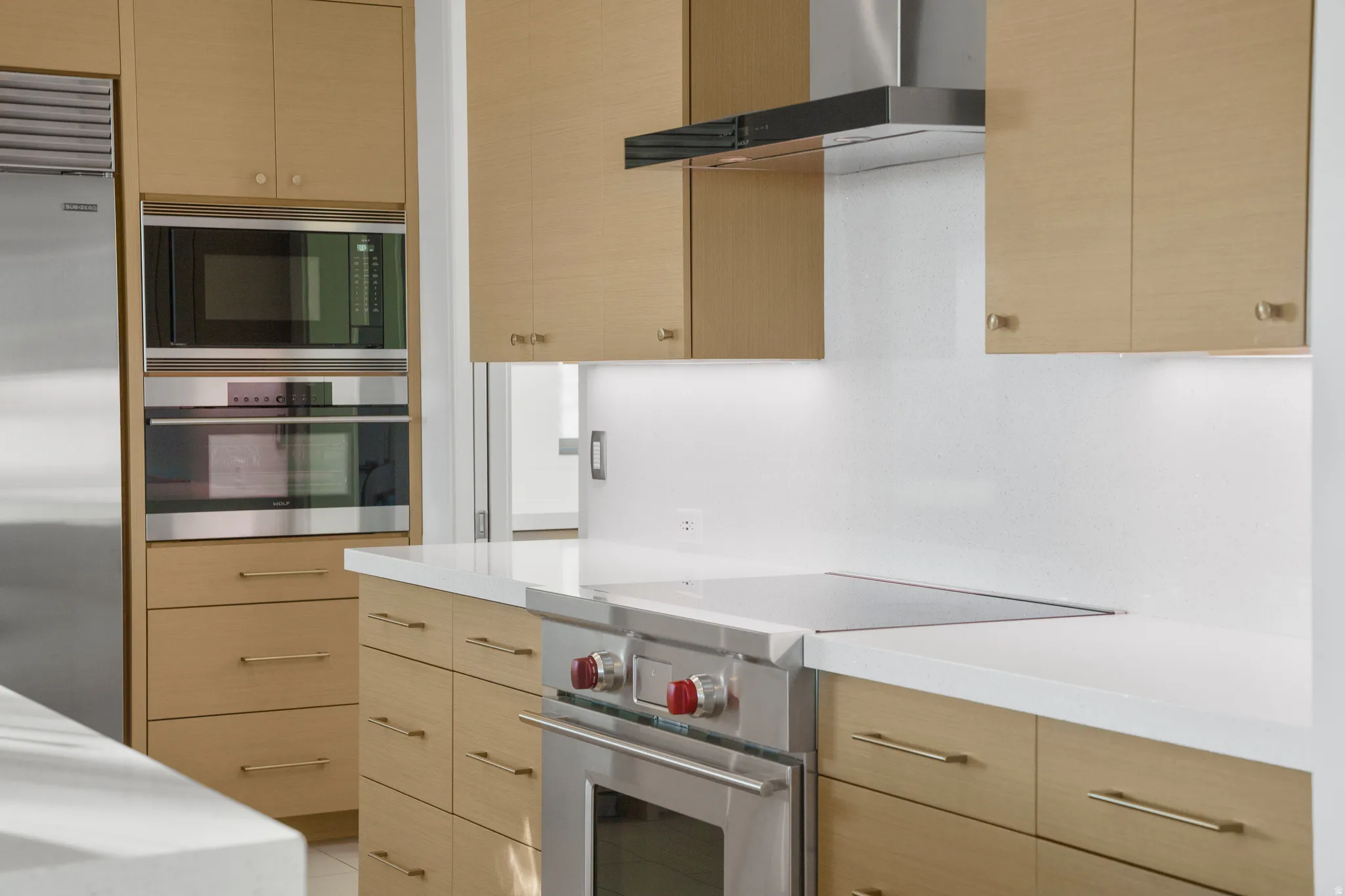 Kitchen with light wood finish cabinets, built in appliances, and modern cabinets