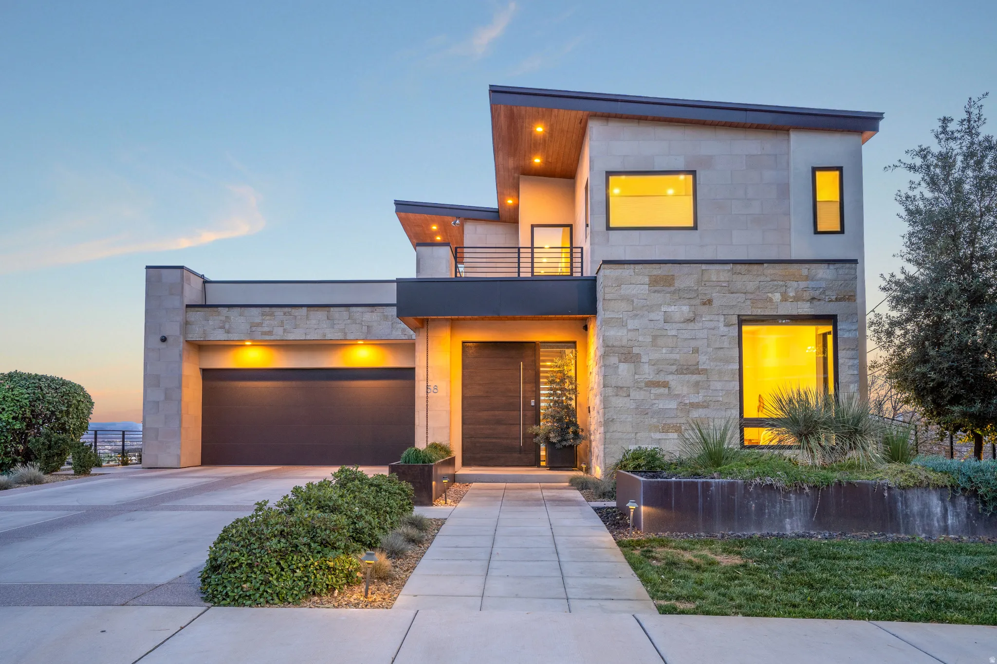 Modern home with a balcony, concrete driveway, stone siding, and a garage