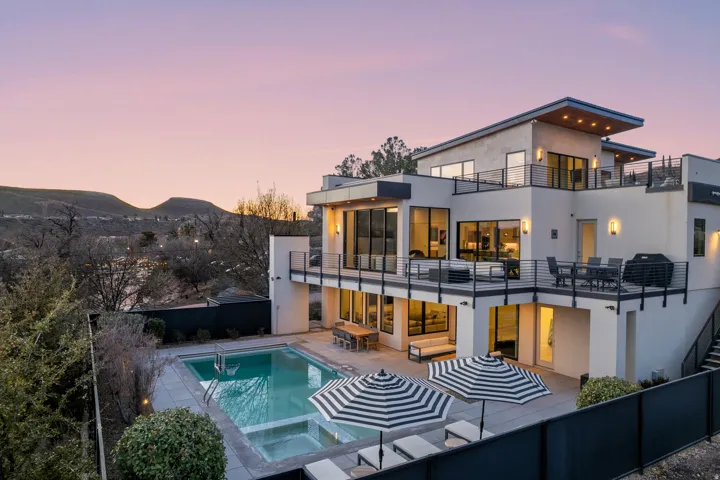 Rear view of house with a patio, stucco siding, a pool with connected hot tub, a balcony, and a mountain view