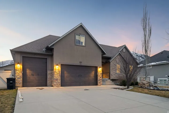 View of front of house featuring stone siding, a shingled roof, driveway, an attached garage, and stucco siding