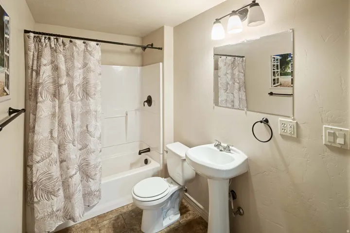 Bathroom with shower / bathtub combination with curtain, a textured wall, and a textured ceiling