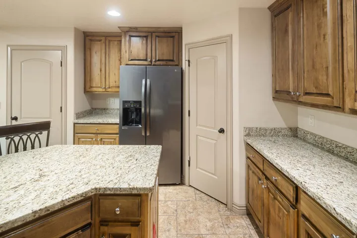 Kitchen featuring stainless steel fridge with ice dispenser, light stone countertops, recessed lighting, and wood finish cabinets