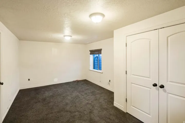 Unfurnished bedroom featuring a textured ceiling, dark carpet, and a closet