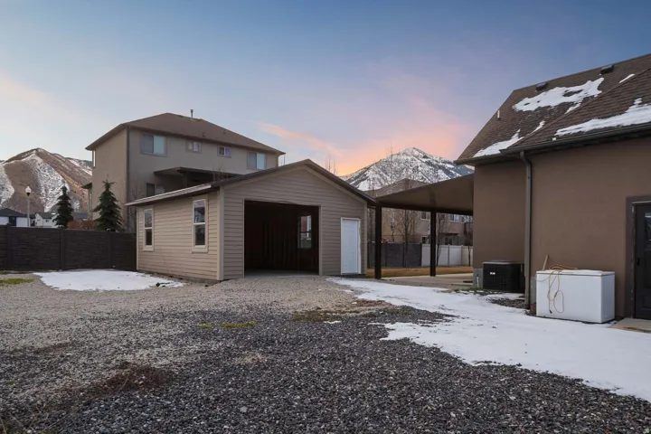 Snow covered property with an outdoor structure, stucco siding, a patio, a garage, and a mountain view