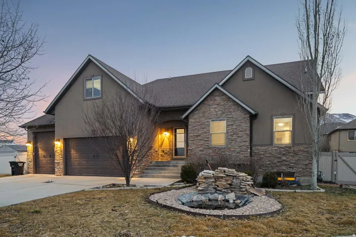 View of front of property with stone siding, driveway, stucco siding, roof with shingles, and a front yard