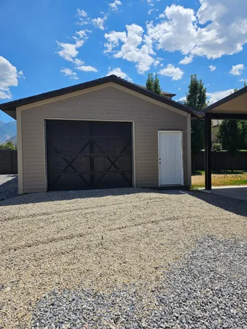 Detached garage structure featuring horizontal siding, a single black garage door with decorative cross-bracing, and a white side entry door