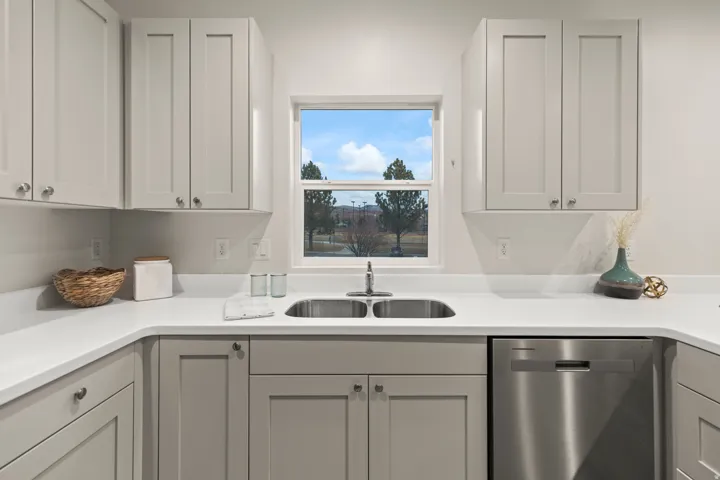 Kitchen featuring stainless steel dishwasher, light countertops, white cabinetry, and gray cabinetry