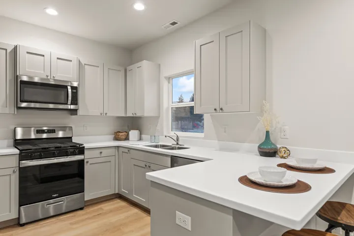 Kitchen featuring stainless steel appliances, a peninsula, a kitchen bar, light countertops, and light wood-style floors