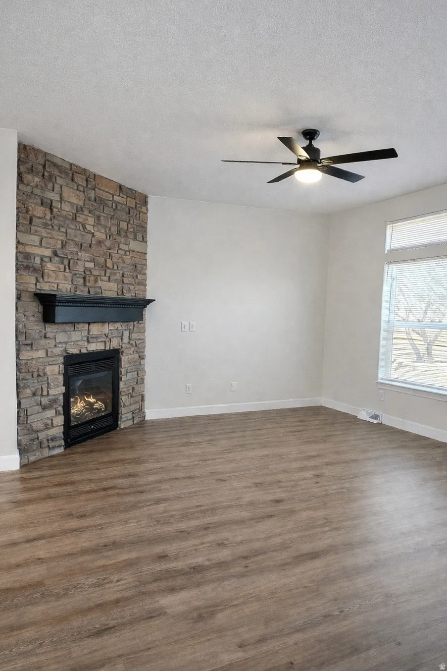 Unfurnished living room with a fireplace, dark wood-style flooring, ceiling fan, and a textured ceiling