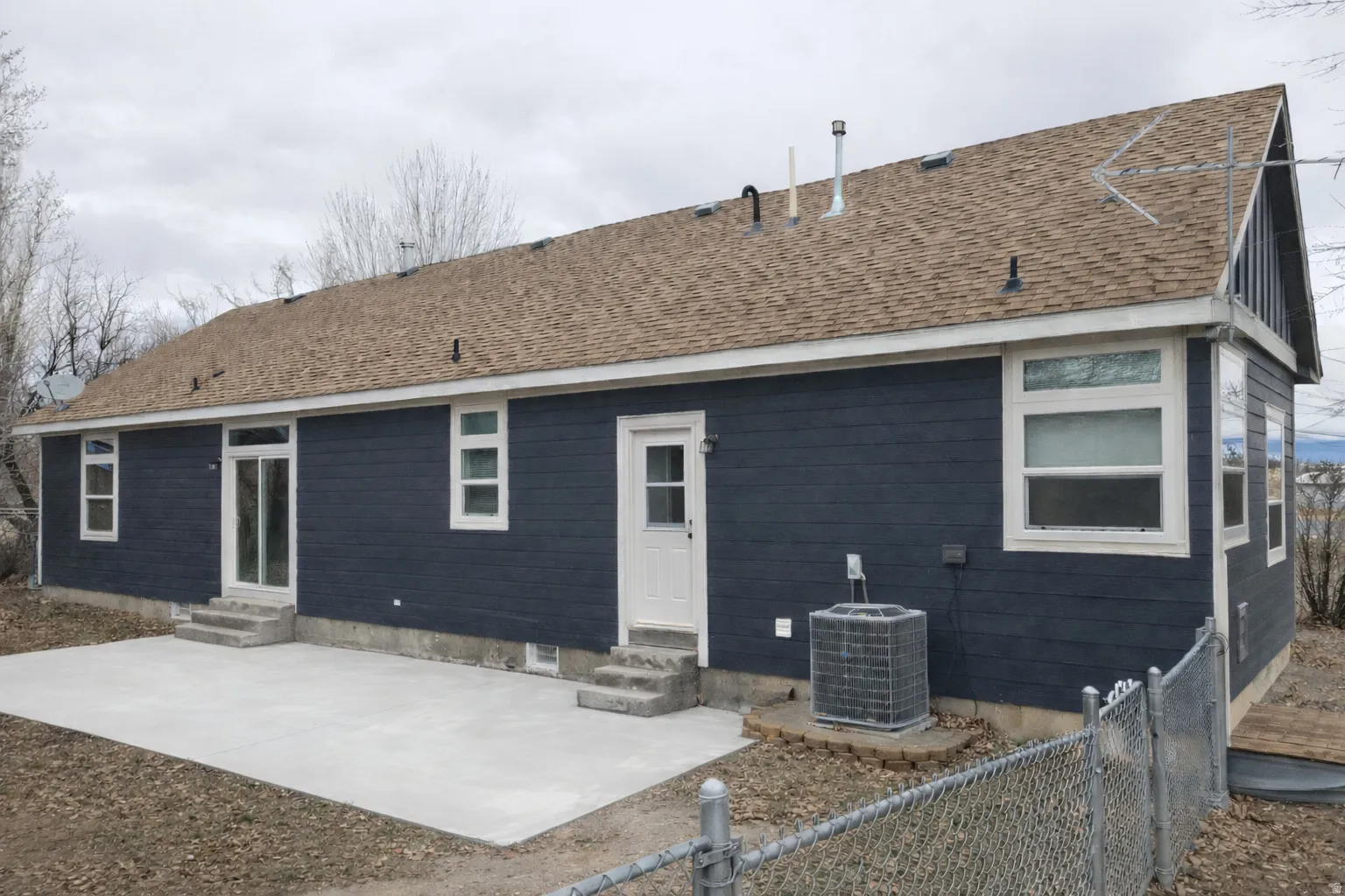 Rear view of house featuring entry steps, a patio, and a shingled roof