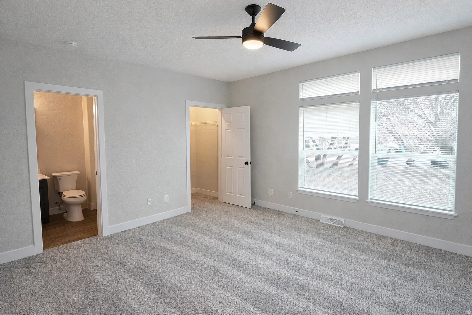 Unfurnished bedroom featuring a walk in closet, light carpet, ceiling fan, and connected bathroom