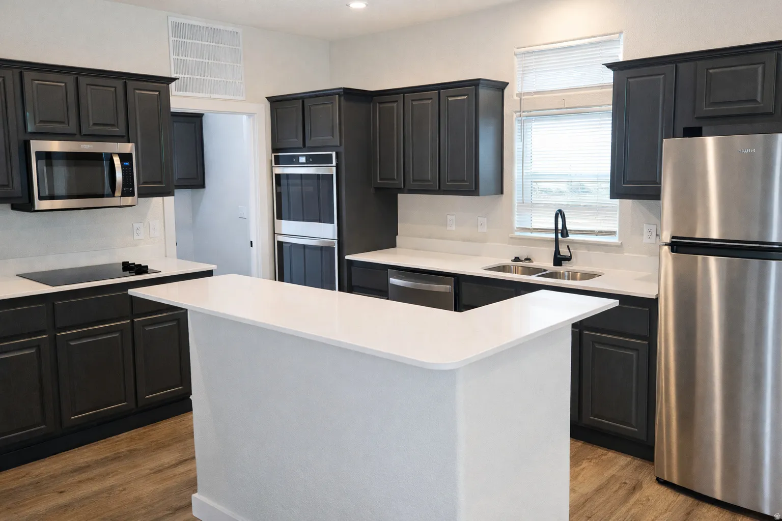 Kitchen with stainless steel appliances, light wood-type flooring, a kitchen island, light stone counters, and dark cabinets